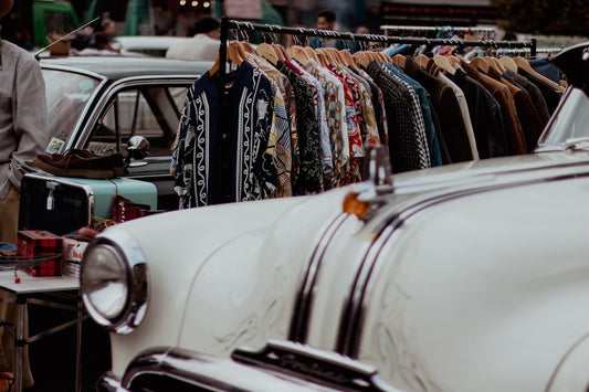 estimer valeur vêtement vintage - a man standing next to a white car in front of a row of shirts