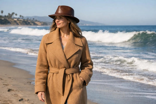 Manteau femme élégant hiver californien 2026, femme en manteau camel sur plage ensoleillée.